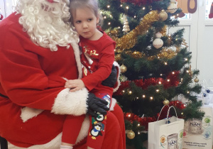 Mikołaj trzyma na kolanach dziewczynkę.